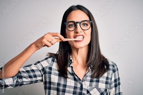 Young caucasian woman wearing glasses brushing her teeth using tooth brush and oral paste  cleaning teeth and tongue as healthy health care morning routine