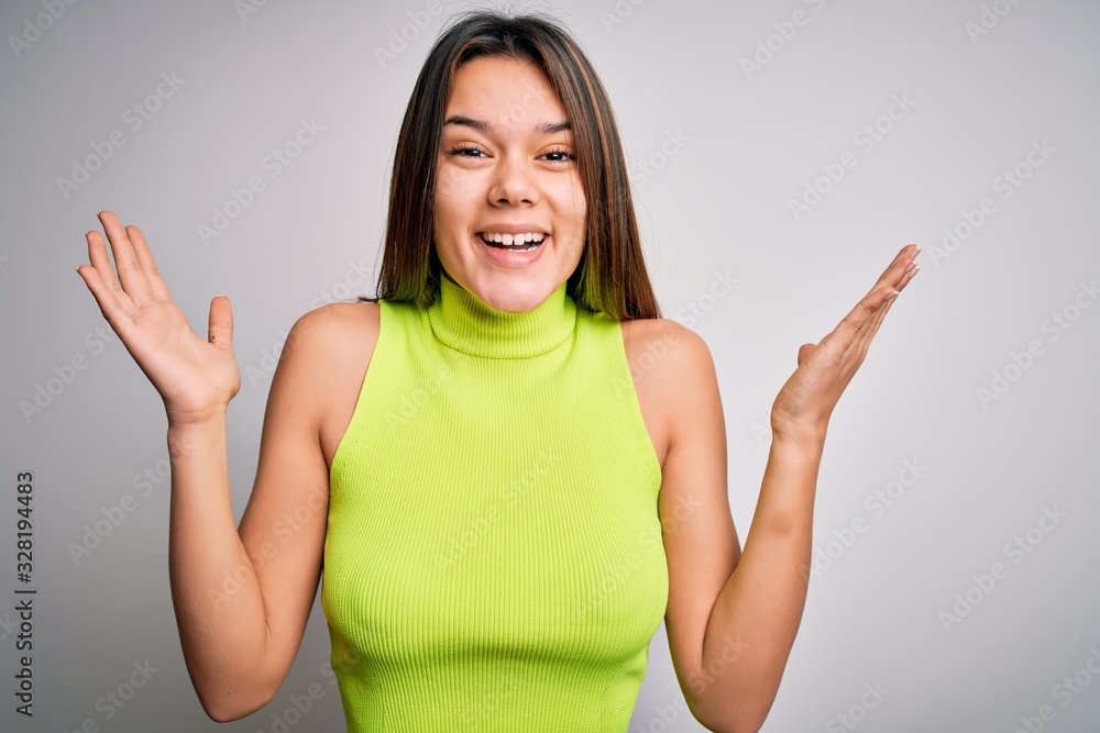 Young beautiful brunette girl wearing casual summer t-shirt over isolated white background celebrating crazy and amazed for success with arms raised and open eyes screaming excited. Winner concept Young beautiful brunette girl wearing casual summer t-shirt over isolated white background celebrating crazy and amazed for success with arms raised and open eyes screaming excited. Winner concept