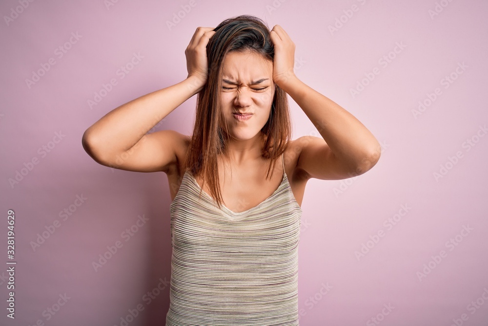 Young beautiful brunette girl wearing casual striped t-shirt over isolated pink background suffering from headache desperate and stressed because pain and migraine. Hands on head. Young beautiful brunette girl wearing casual striped t-shirt over isolated pink background suffering from headache desperate and stressed because pain and migraine. Hands on head.