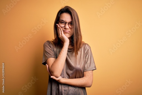 Beautiful brunette girl wearing casual t-shirt and glasses over isolated yellow background thinking looking tired and bored with depression problems with crossed arms.