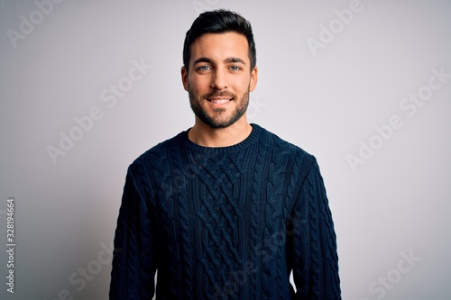 Young handsome man with beard wearing casual sweater standing over white background with a happy and cool smile on face. Lucky person.