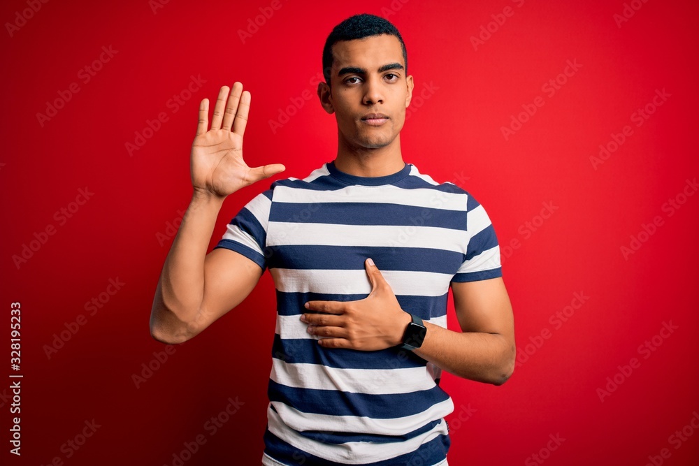 Handsome african american man wearing casual striped t-shirt standing over red background Swearing with hand on chest and open palm, making a loyalty promise oath Handsome african american man wearing casual striped t-shirt standing over red background Swearing with hand on chest and open palm, making a loyalty promise oath