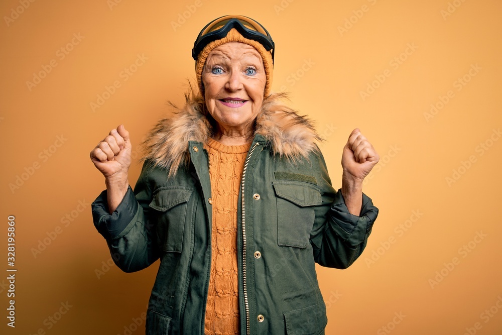 Senior beautiful grey-haired skier woman wearing snow sportswear and ski goggles celebrating surprised and amazed for success with arms raised and open eyes. Winner concept.