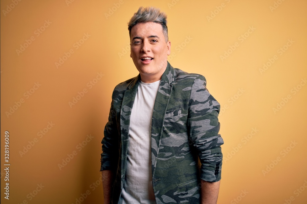 Fototapeta premium Young handsome modern man wearing business jacket standing over yellow isolated background winking looking at the camera with sexy expression, cheerful and happy face.