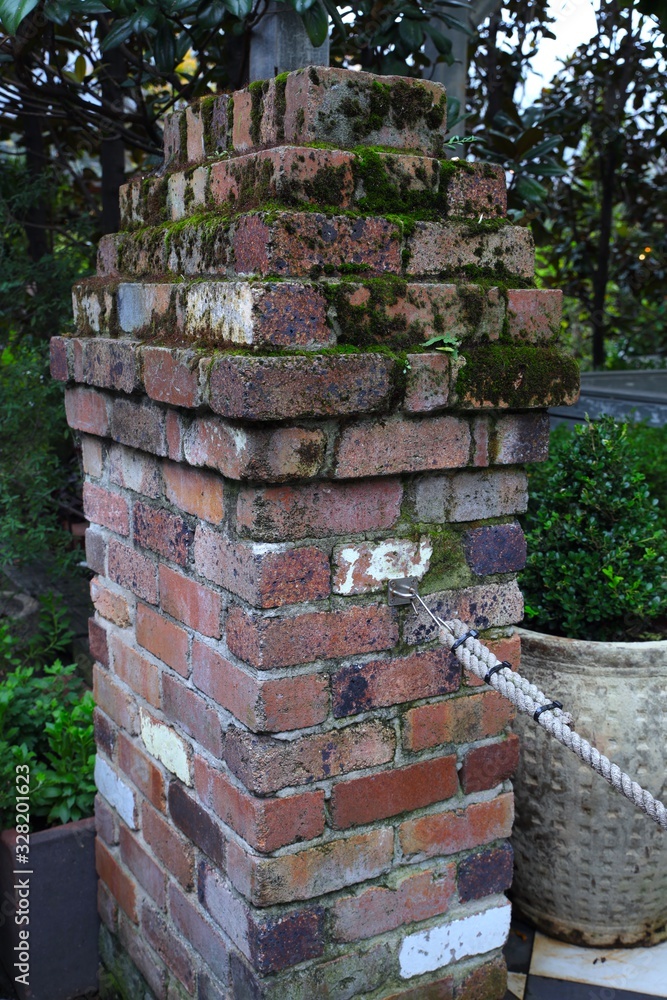 Old brick column with green mould ground all over has an old rustic look in a garden in Sydney NSW Australia
