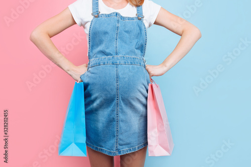 A pensive, confused pregnant woman holds a pink bag for a girl and a blue one for a boy. Choosing the child's gender