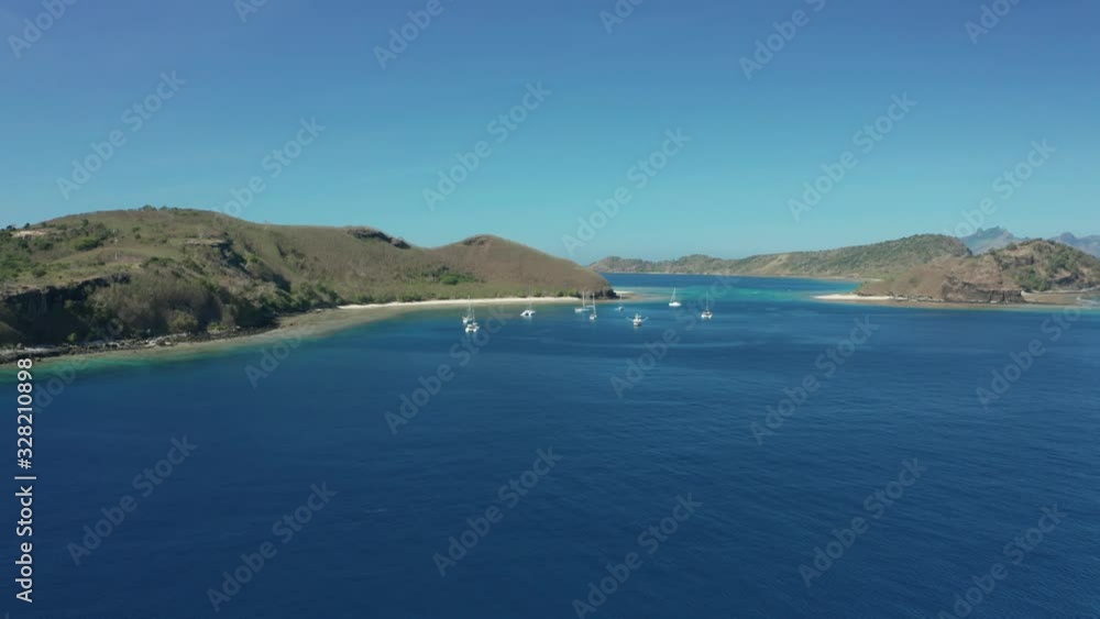 Fiji Islands - Sailboats Adrift Over The Dark Blue Ocean Water Surrounding The Green Island Under The Clear Blue Sky - Wide Shot Fiji Islands - Sailboats Adrift Over The Dark Blue Ocean Water Surrounding The Green Island Under The Clear Blue Sky - Wide Shot