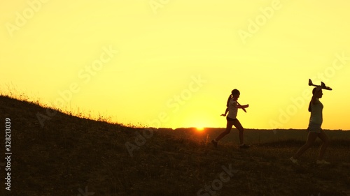 Dreams of flying. Happy childhood concept. Two girls play with a toy plane at sunset. Children on background of sun with an airplane in hand. Silhouette of children playing on plane
