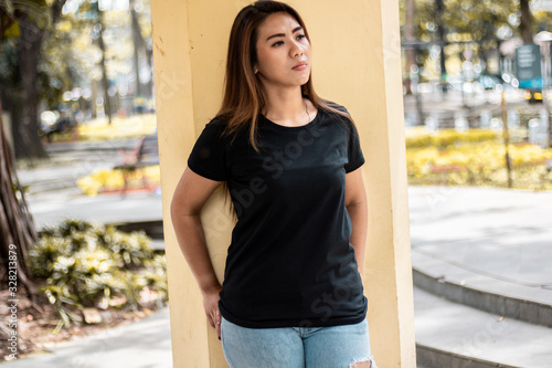 Woman wearing black t shirt posing at park in front view, suitable for mock up template, background, etc.