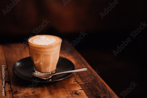 Mug of flat white coffee with latte art on wooden table at the hipster coffee shop. Copyspace, Low-key lighting.