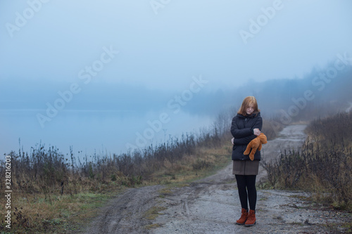 Sad teenager girl with  teddy bear on country road by foggy  lake.  Concept of adolescence and adolescent problems. © Maya Kruchancova