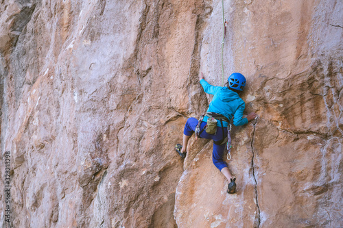 A woman in a helmet climbs a beautiful orange rock.