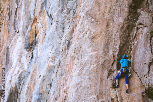 A woman in a helmet climbs a beautiful orange rock.