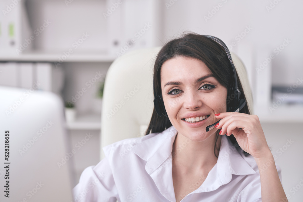 Portrait of smiling friendly helpdesk operator adjusting microphone headset while communicating with customer Portrait of smiling friendly helpdesk operator adjusting microphone headset while communicating with customer