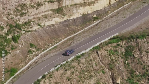 Blue SUV car driving alone on asphalt winding zig zag empty serpentine road and mid shot famous Caucasus Dzhily Su freeway at summer sunny day - Aerial drone view photo