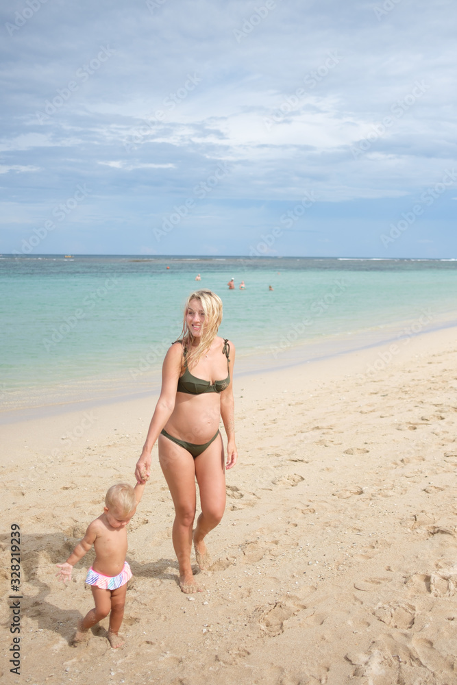 Beautiful portrait of mother and daughter on the sea and beach background. Happy family in vacation. Travel. Caucasian female with baby outside at ocean. Motherhood care. Beautiful portrait of mother and daughter on the sea and beach background. Happy family in vacation. Travel. Caucasian female with baby outside at ocean. Motherhood care.