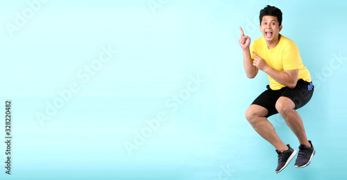 Fototapeta Naklejka Na Ścianę i Meble -  Smiling joyful asian man jumping and Pointing finger on empty space. isolated on blue background in studio With copy space.