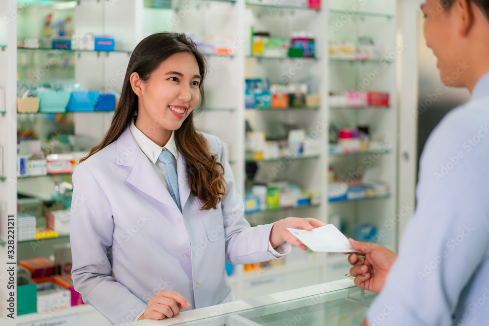 Confident Asian young female pharmacist with a lovely friendly smile and receive medicine prescription from man patient in the pharmacy drugstore. Medicine, pharmaceutics, health care