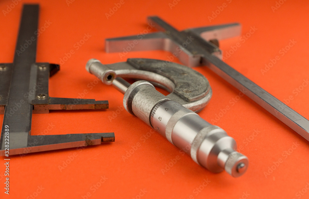 Close-up measuring instrument micrometer, vernier caliper, depth gauge on a bright orange background, some objects are out of focus. Ultraprecise measuring tool Close-up measuring instrument micrometer, vernier caliper, depth gauge on a bright orange background, some objects are out of focus. Ultraprecise measuring tool