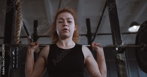 Canvastavla Young beautiful red haired athletic woman straining hard lifting heavy barbell in large professional gym slow motion
