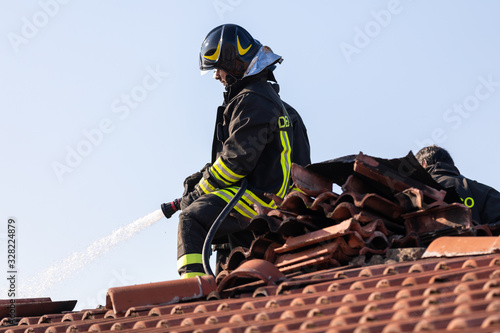 Wallpaper Mural Close up of an Italian fire man standing on a roof and handling a hose to extinguish a smoldering tile Torontodigital.ca