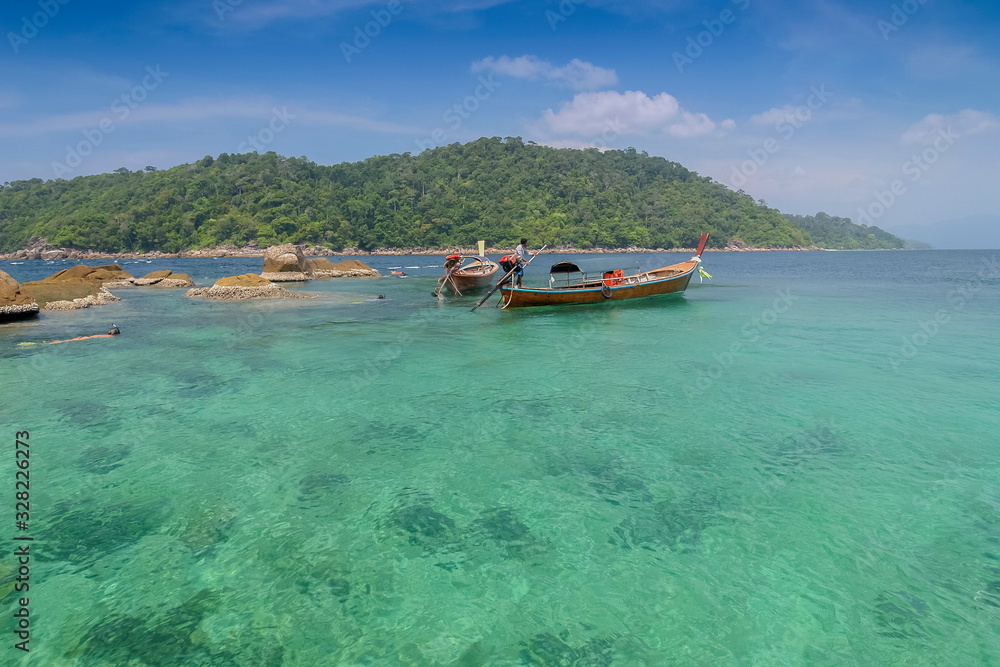 view of tourists snorkeling in blue-green sea and a long-tail boat floating with blue sky background, Ko Jabang, long-tail boat trip from Lipe island, Satun, southern Thailand.