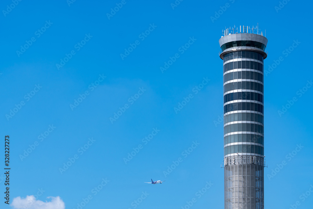 Air traffic control tower in the airport with international flight plane flying on clear blue sky. Airport traffic control tower for control airspace by radar. Aviation technology. Flight management. Air traffic control tower in the airport with international flight plane flying on clear blue sky. Airport traffic control tower for control airspace by radar. Aviation technology. Flight management.