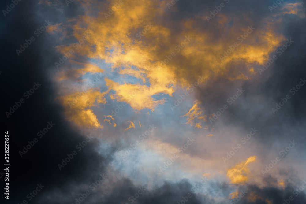 Beautiful golden fluffy thunderclouds illuminated by disappearing rays at sunset and dark clouds floating across sky to change season weather. Natural abstract meteorology background.