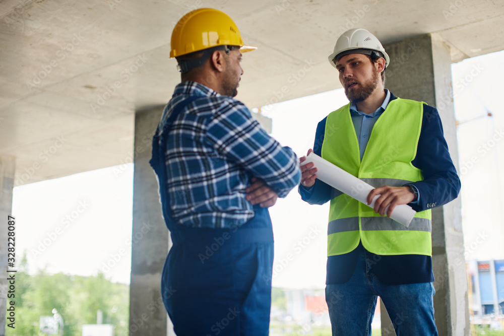Two engineers discuss work related questions together holding folded blueprint. Two engineers discuss work related questions together holding folded blueprint.