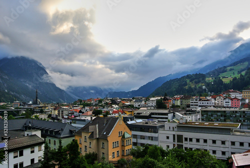 Landeck, Austria - An orange house next to the white houses in a small town, amid green alpine mountains covered with forest, gray clouds in the sky, in the summer afternoon. © Ivars