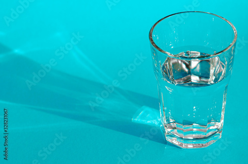 A glass with clean clear clear water stands on a blue background with green shadows. Clean water