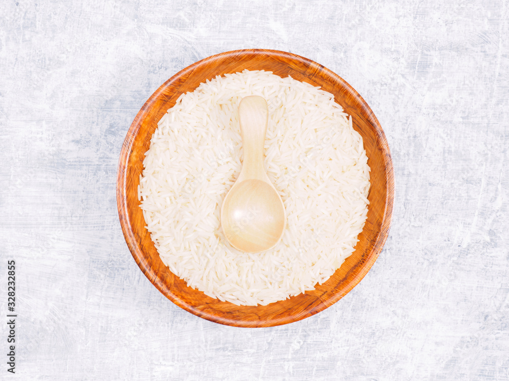 Indian long grain Basmati rice in brown wooden bowl and spoon on white concrete background Indian long grain Basmati rice in brown wooden bowl and spoon on white concrete background