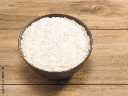 Long grain Basmati rice in brown ceramic bowl on brown wooden background