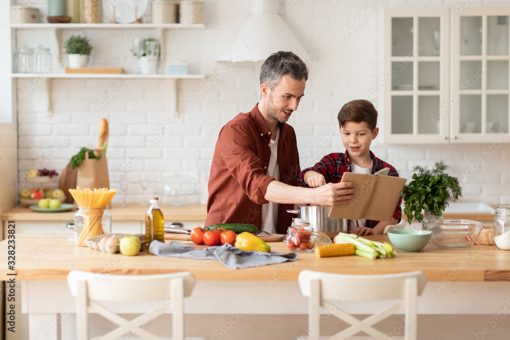 Son and dad reading recipe book and cooking