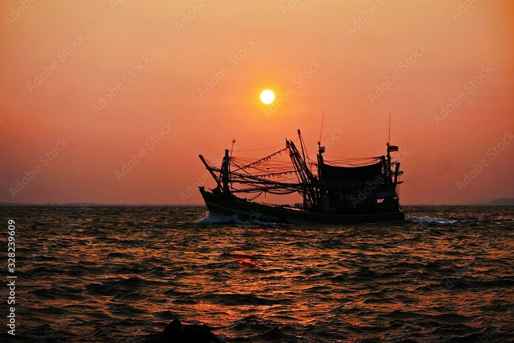The fishing boat returned to the shore at dawn with the sun.