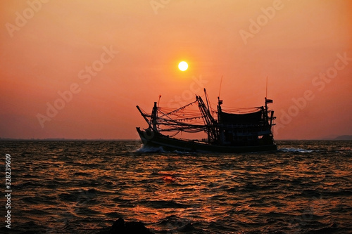 The fishing boat returned to the shore at dawn with the sun.