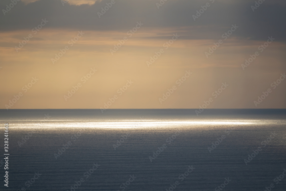 Long aerial view of evening clouds over Tasman sea coast at Piha beach with bright sun spot on ocean surface