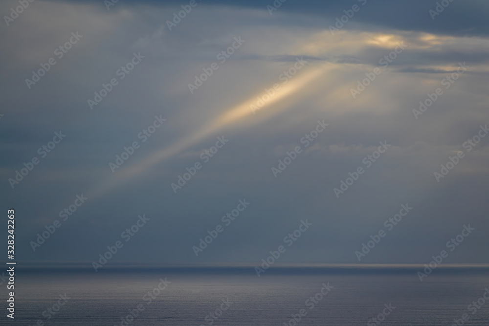 Long aerial view of sun rays penetrating gray evening clouds over Tasman sea coast at Piha beach