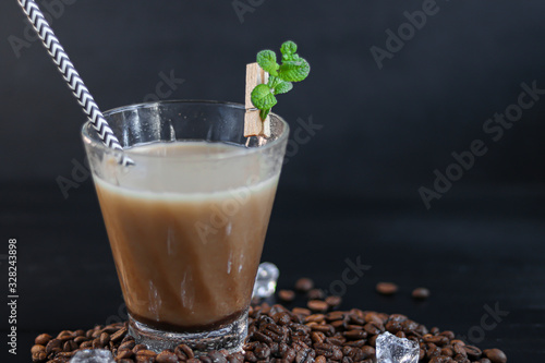 Iced coffee in a tall glass with milk and pieces of ice. On a dark background.