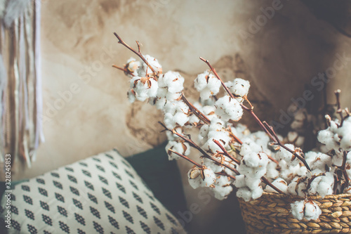 Green blanket on the double bed in stylish wabi sabi rustic bedroom of minimal style house, feathers hanging from the ceiling and cotton bouquet in a basket