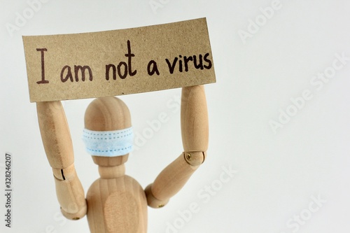 Cardboard sign with text I am not a virus in the hands of a wooden doll or mannequin in a medical mask. Concept of anti racism, anti xenophobia, the social situation around the Coronavirus or Covid-19
