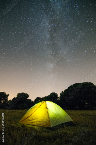 Tienda de campaña de noche en medio del campo y fondo de estrellas y la vía láctea de fondo.