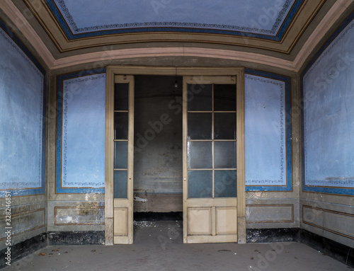 Puerta acristalada de entrada de habitación azul con cenefas de casa abandonada.