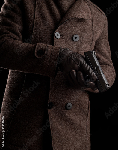 A man in a dark coat holds a gun. Security guard or bodyguard with arms in hand.