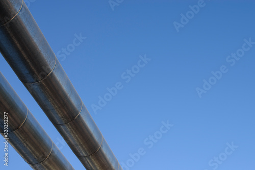 Two metal pipes diagonally. Chrome stainless steel. Blue sky background. Concept of the gas pipeline, oil pipeline, fuel pipe, conduit.