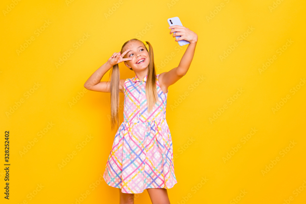 Photo of pretty small lady hold telephone young influencer making selfies for blog showing v-sign symbol near eye wear checkered summer dress isolated bright color background Photo of pretty small lady hold telephone young influencer making selfies for blog showing v-sign symbol near eye wear checkered summer dress isolated bright color background