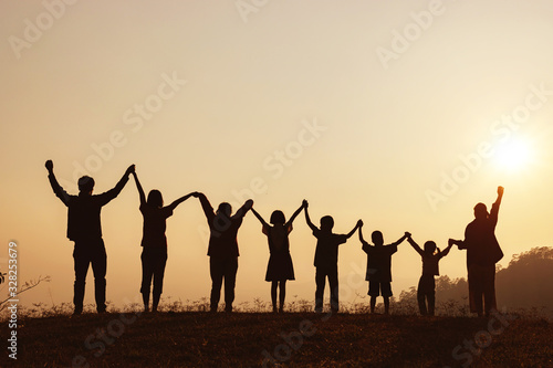 Silhouette of happy family standing with raised hands on the mountain at the sunset time.