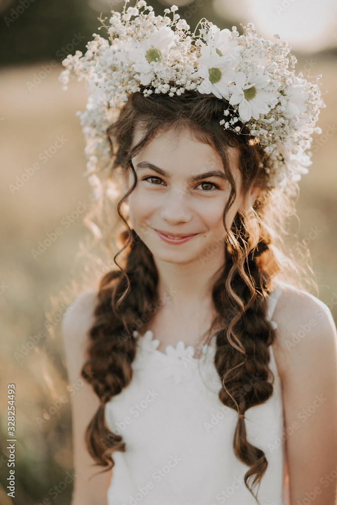 portrait of a smiling young girl in a white dress and a floral wreath on her hair with braids in the summer field portrait of a smiling young girl in a white dress and a floral wreath on her hair with braids in the summer field