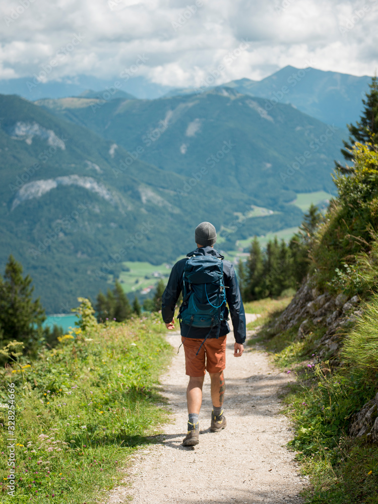 Man with backpack hiking in forested mountains walking by footpath during sunny day