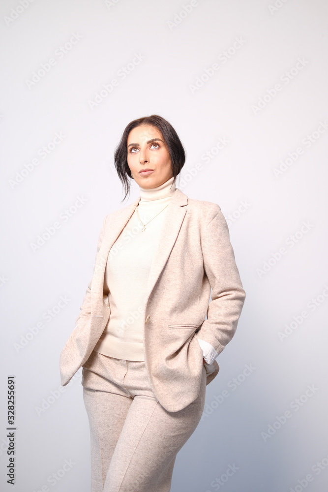 Portrait of a smiling mid-aged business woman in a light milk-colored trouser suit and turtleneck against a light wall. Portrait of a smiling mid-aged business woman in a light milk-colored trouser suit and turtleneck against a light wall.